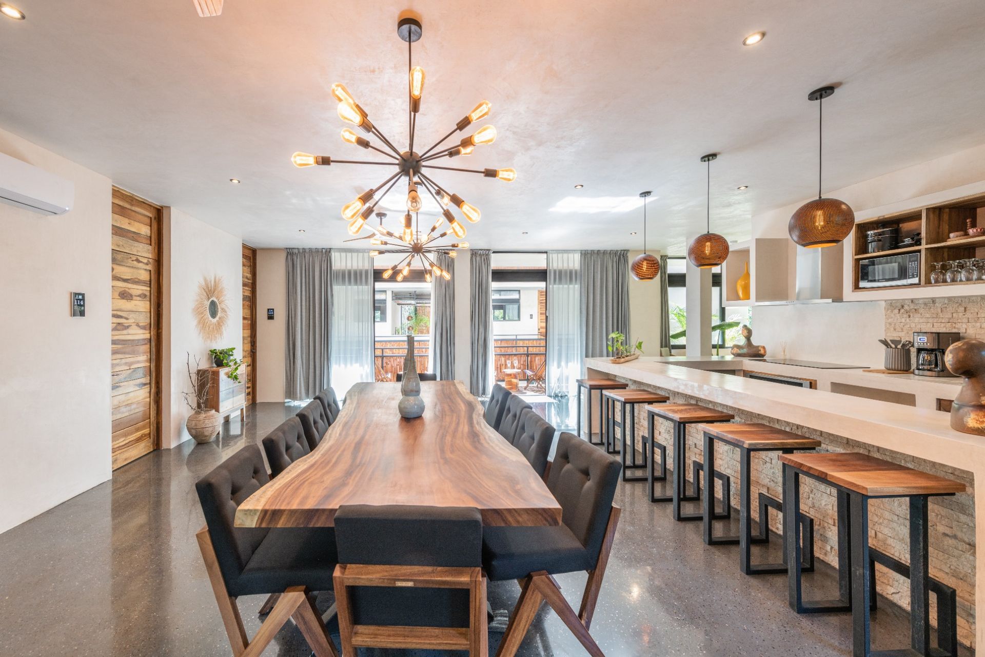 Modern dining room with a long wooden table, chairs, and a kitchen with bar seating.