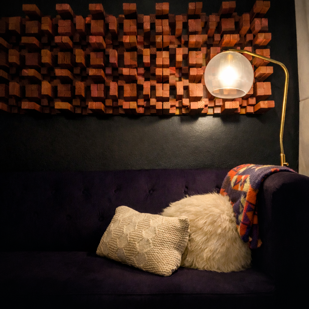 Velvet couch with pillows under a wood wall decor, lit by a midcentury lamp.