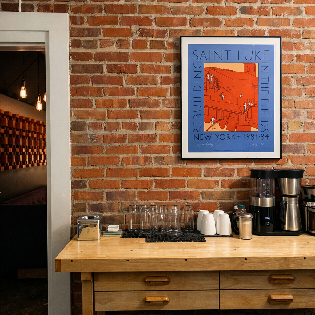 Countertop with coffee maker and glasses on a brick wall with framed poster, near open doorway.