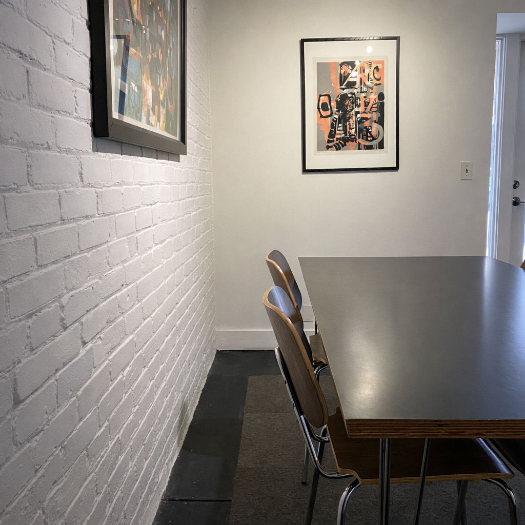 Meeting space with a white brick wall with two framed art pieces, table, and chairs.