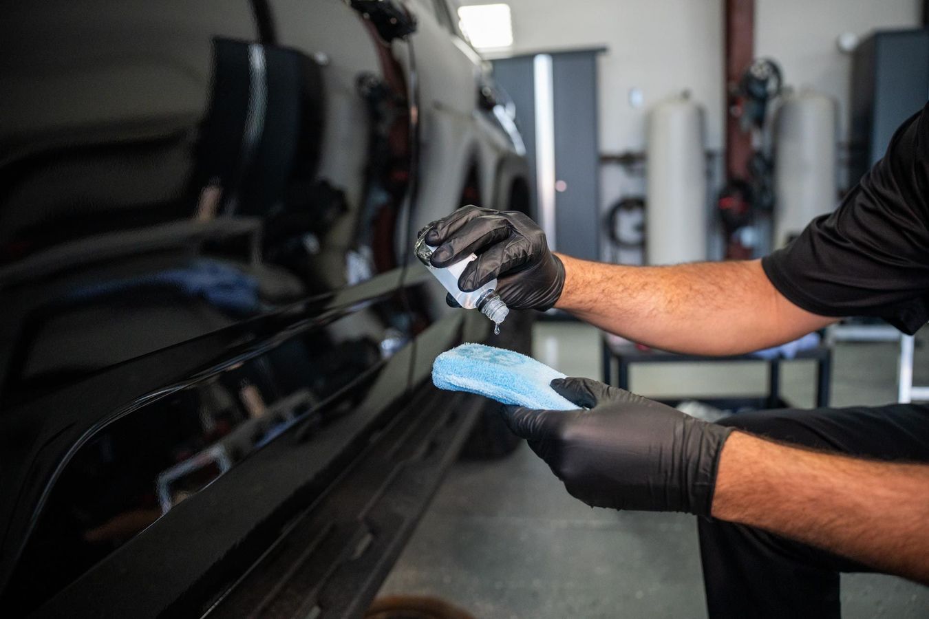 Ceramic Coating - A man wearing black gloves is cleaning a black car with a blue cloth .