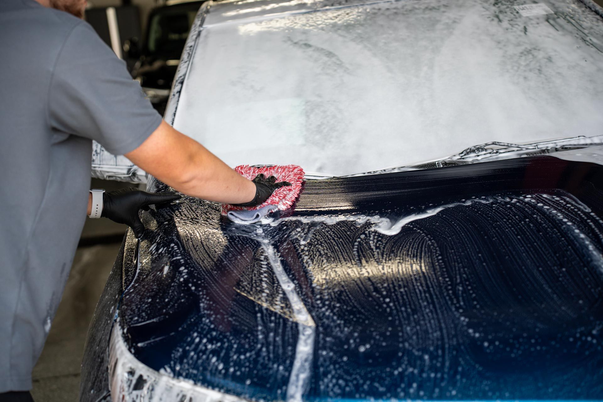 Exterior Detailing - A man is washing a car with a sponge and foam.