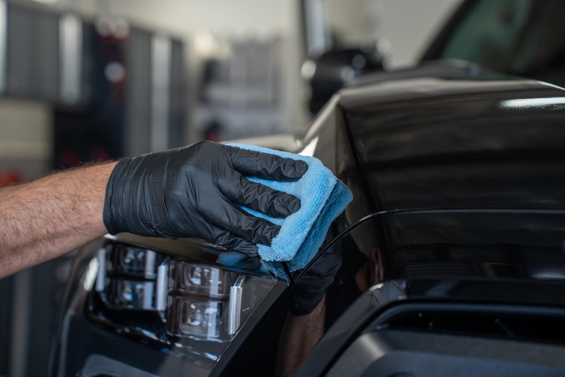 Ceramic Coating - A person wearing black gloves is cleaning a black car with a blue cloth in Fairhaven, MA