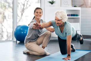 A woman is helping an older woman do push ups on a yoga mat.