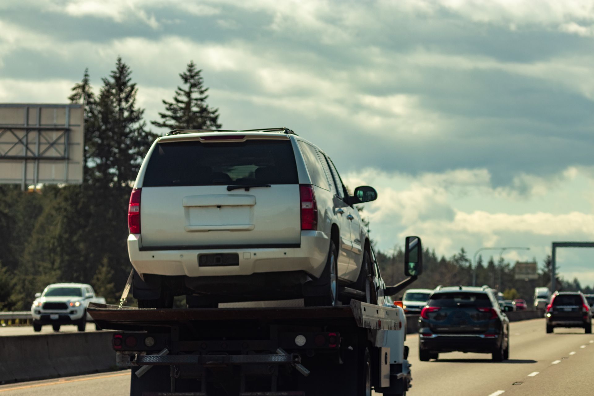 A white suv is being towed down a highway by a tow truck, representing reposession.