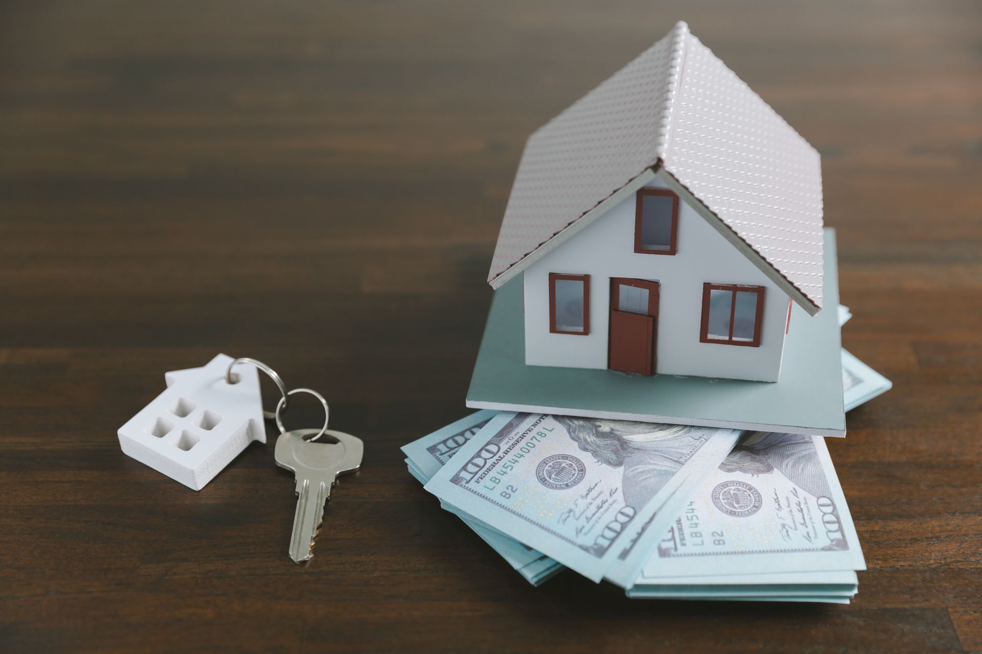 A model house is sitting on top of a pile of money next to a key, representing mortgage modification.