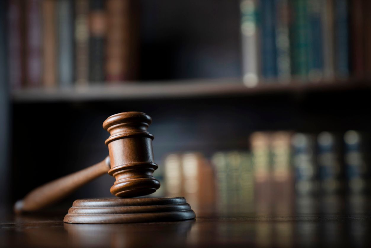 A wooden judge 's gavel is sitting on a wooden table in front of a bookshelf representing the topic of Chater 11 bankruptcy.