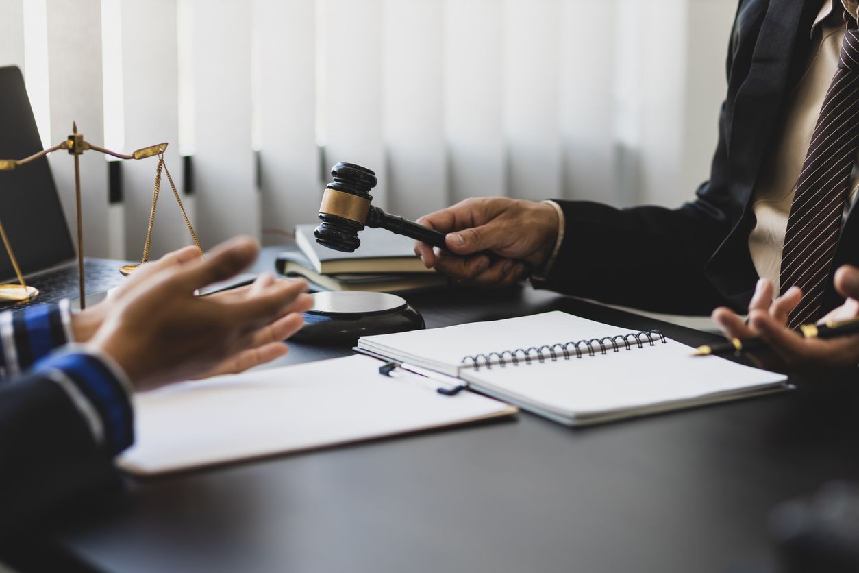 A judge is holding a gavel while sitting at a table with two people.