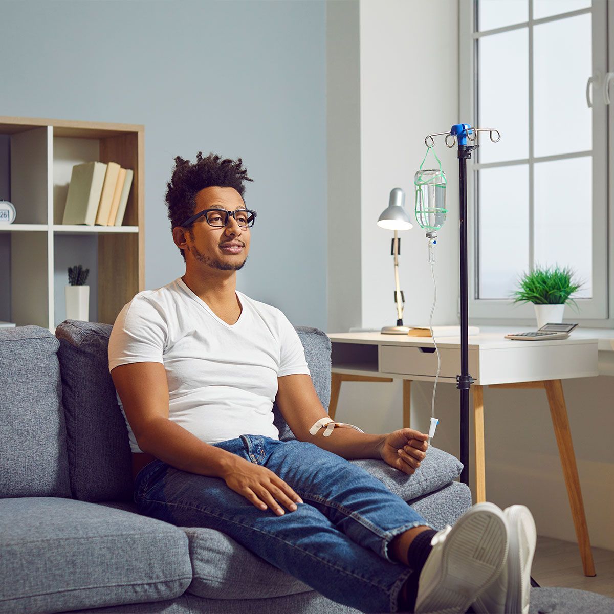 Young man with vitamin deficiency receiving modern intravenous anti stress nutrient and hydration therapy through sterile IV drip line infusion system for healthy body and stress relief