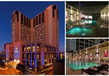 Hilton Hotel exterior and pool area at night. A tall building is next to multiple lit pools.