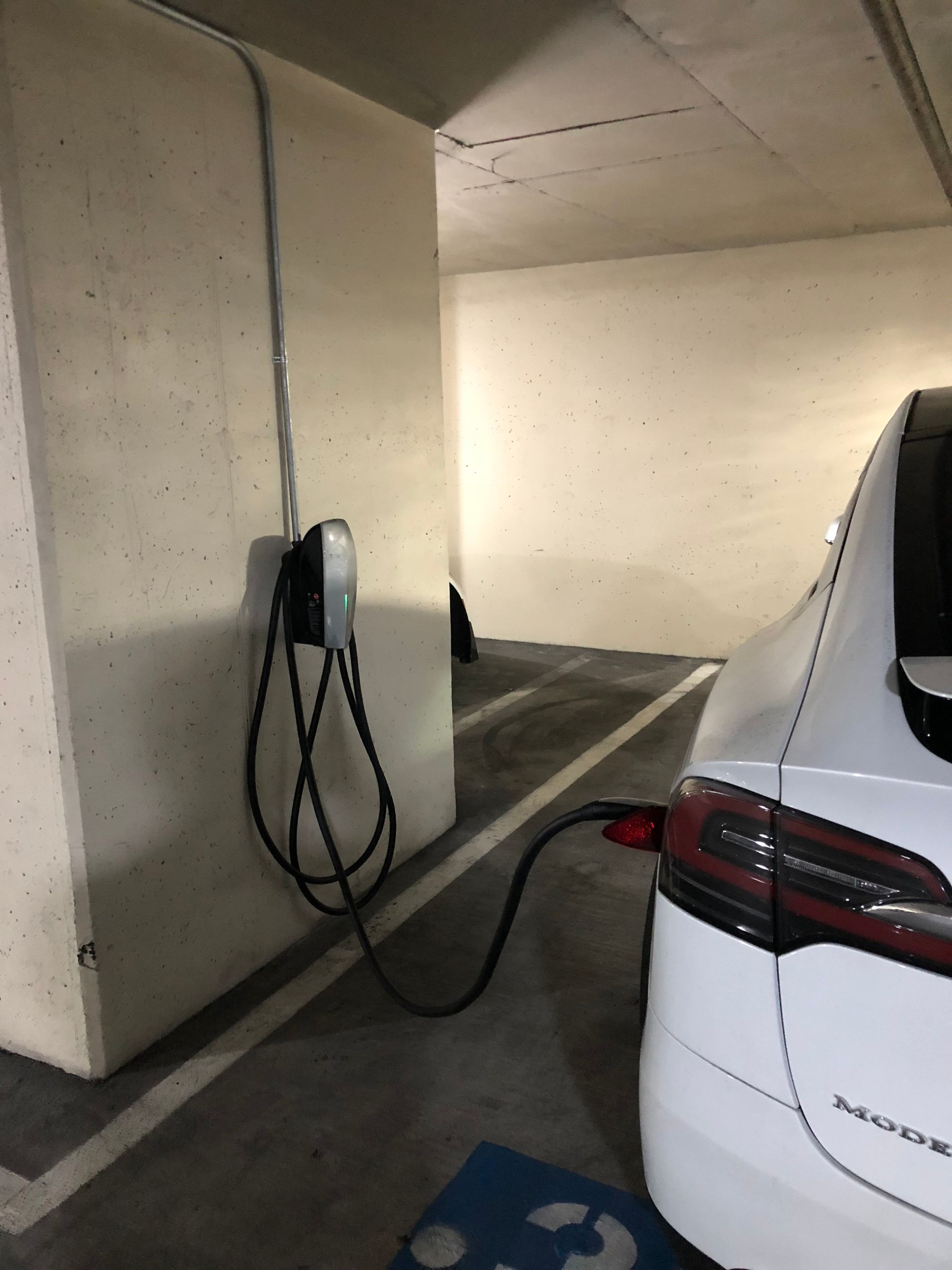 EV charger installation Austin, white Tesla charging on a Level 2 station in a parking garage with a dedicated 240V circuit
