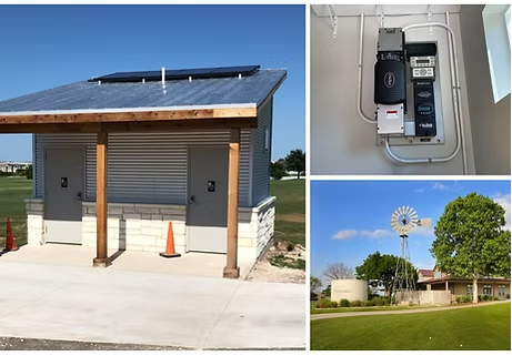 A small restroom building with solar panels and a windmill in a park setting.