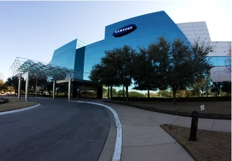 Samsung building with blue glass exterior, trees in front. Asphalt road curves to the entrance.