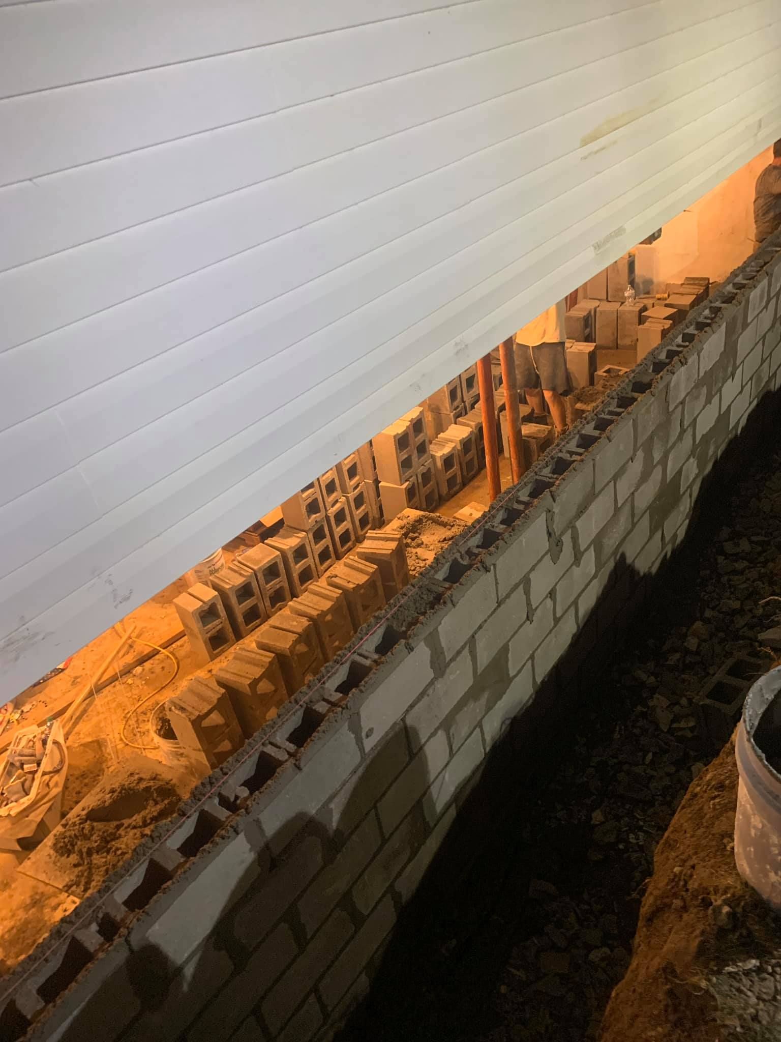 Damaged brick wall with a view of buildings beyond, under a corrugated white roof.