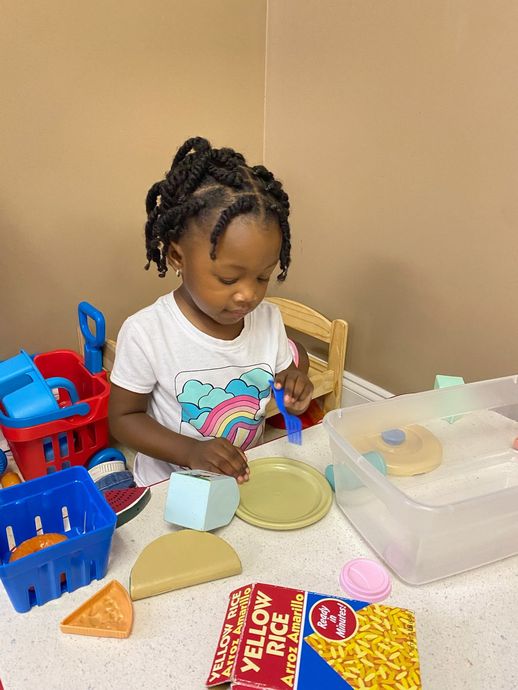 Girl with braided hair playing with toy food on a table.