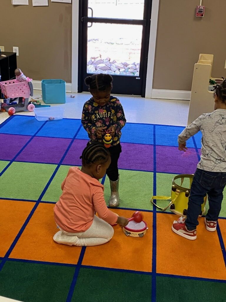Three children playing with toys on a colorful, square-patterned rug indoors.