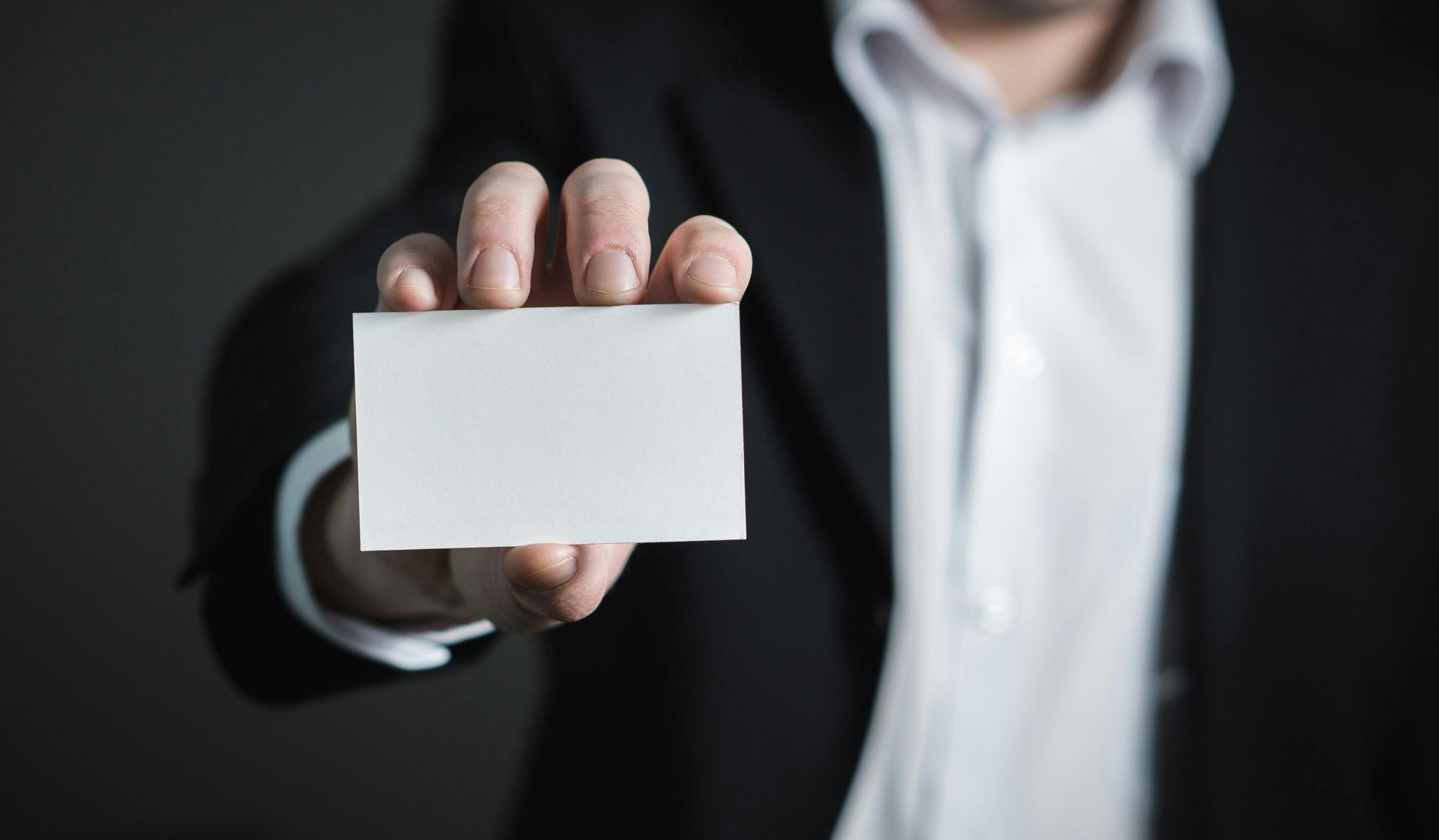 Man in suit holding out a blank business card.