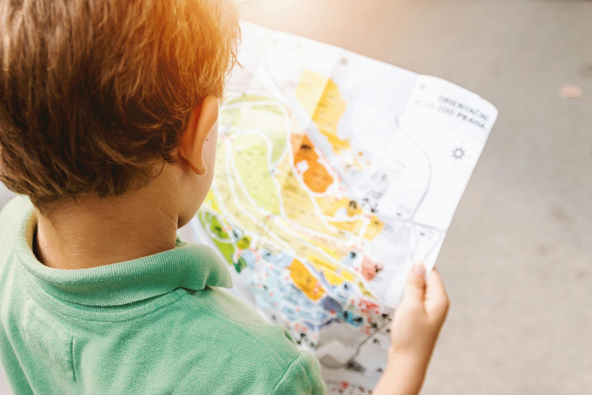 Boy in green shirt looking at a colorful map outdoors.