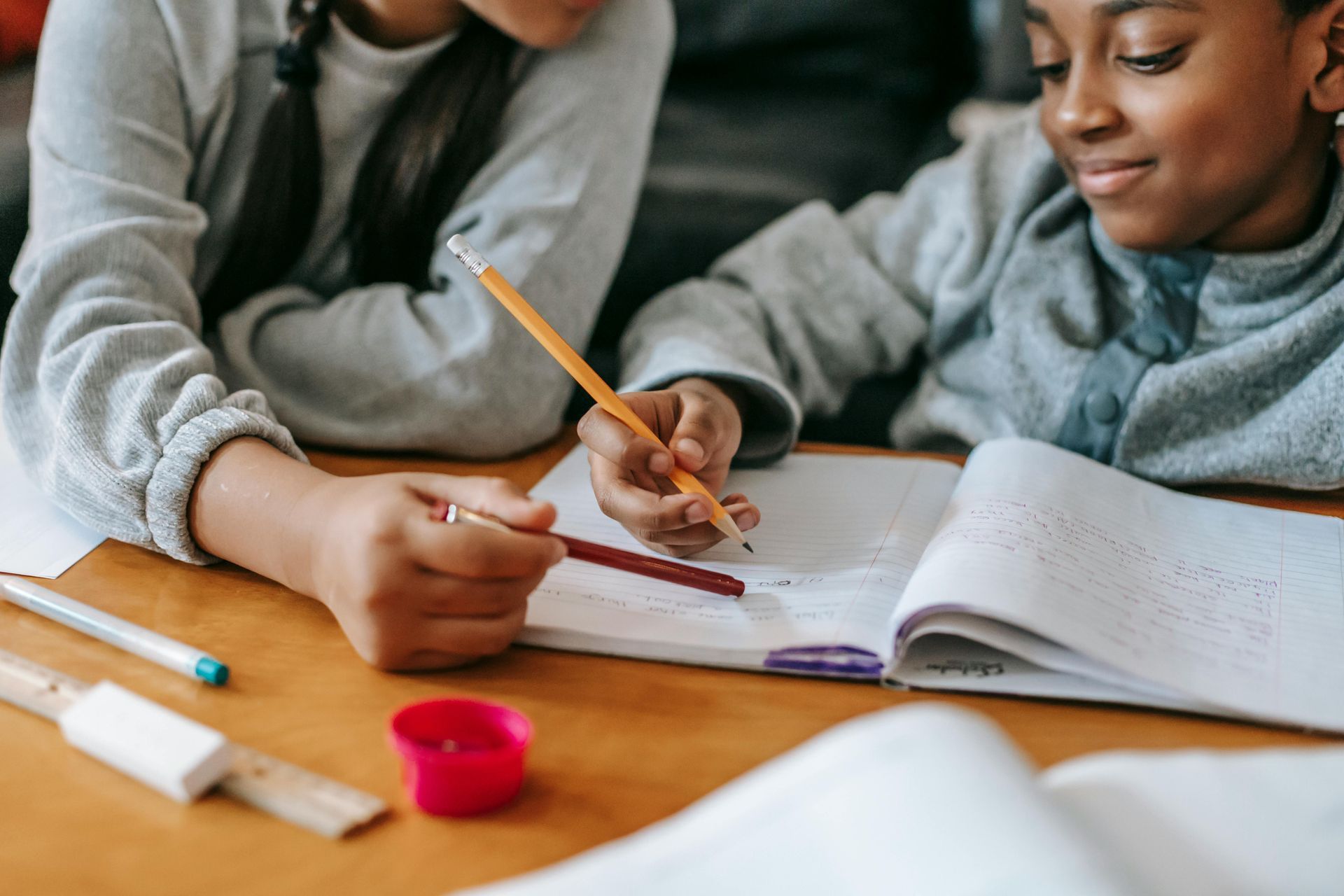 Two children working on homework together at a table, focused and smiling.