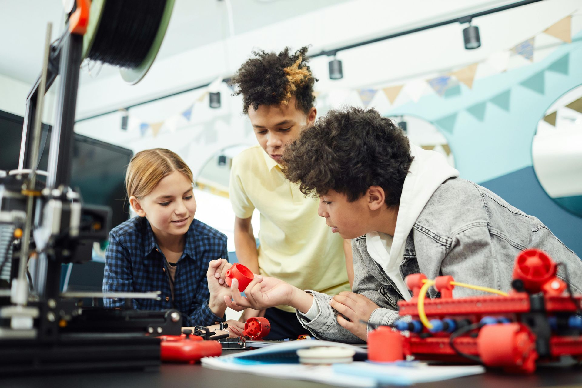 Three young students working together with 3D printed objects and robotics in a classroom.