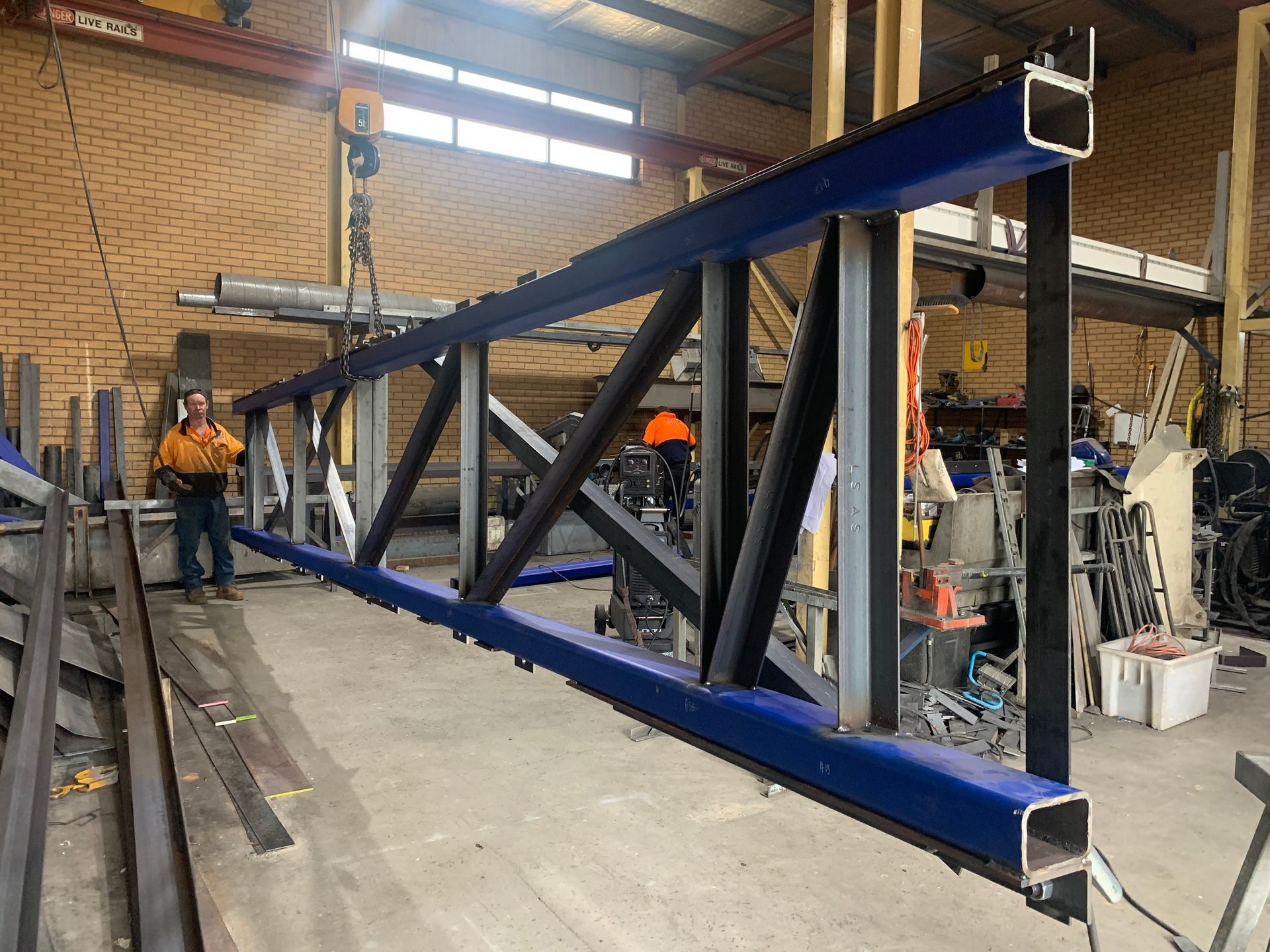 A man is standing next to a blue and black metal structure in a warehouse — Magnum Steel In Crestwood, NSW