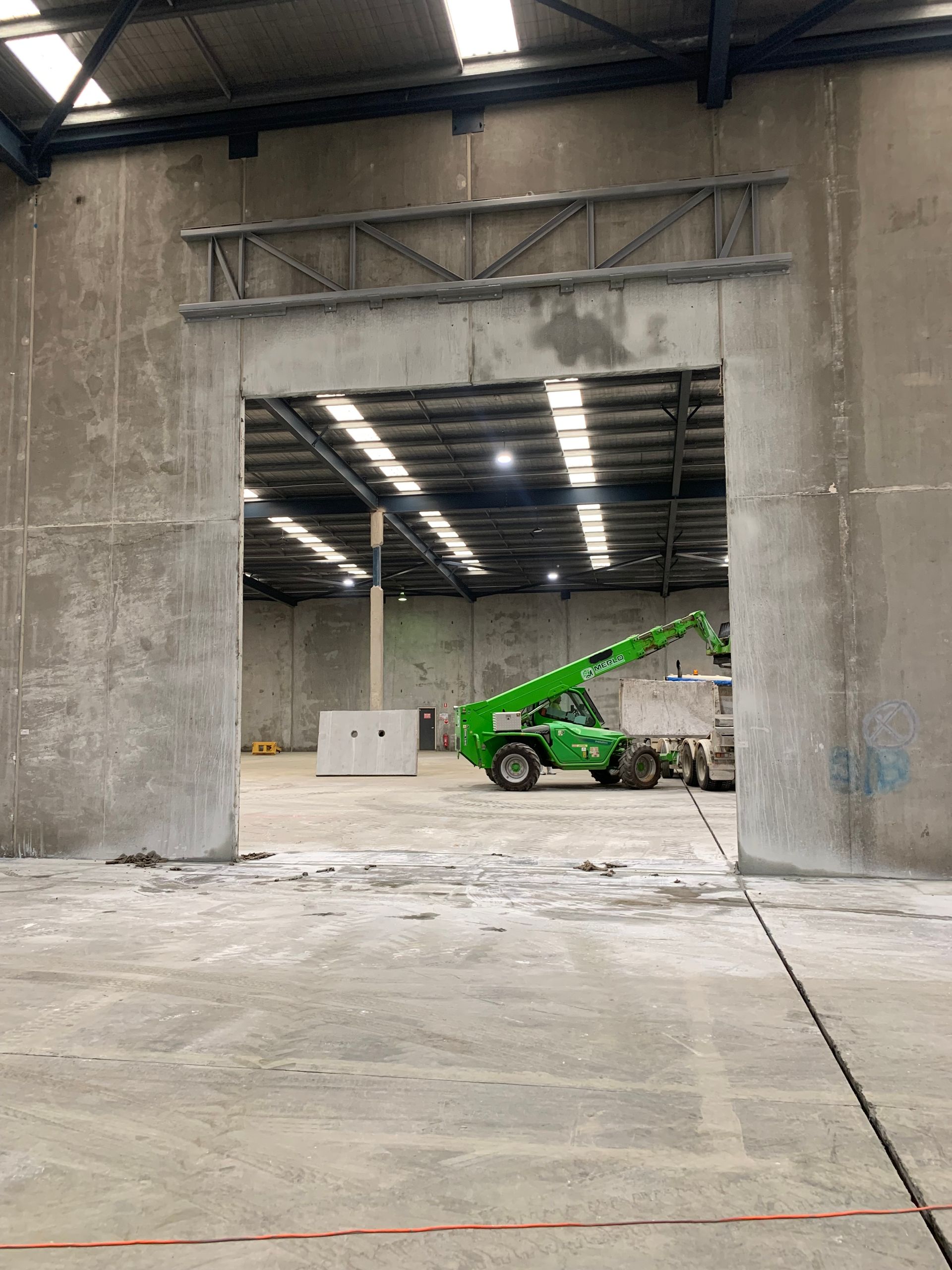 A green crane is cutting a hole in the wall of a warehouse — Magnum Steel In Crestwood, NSW