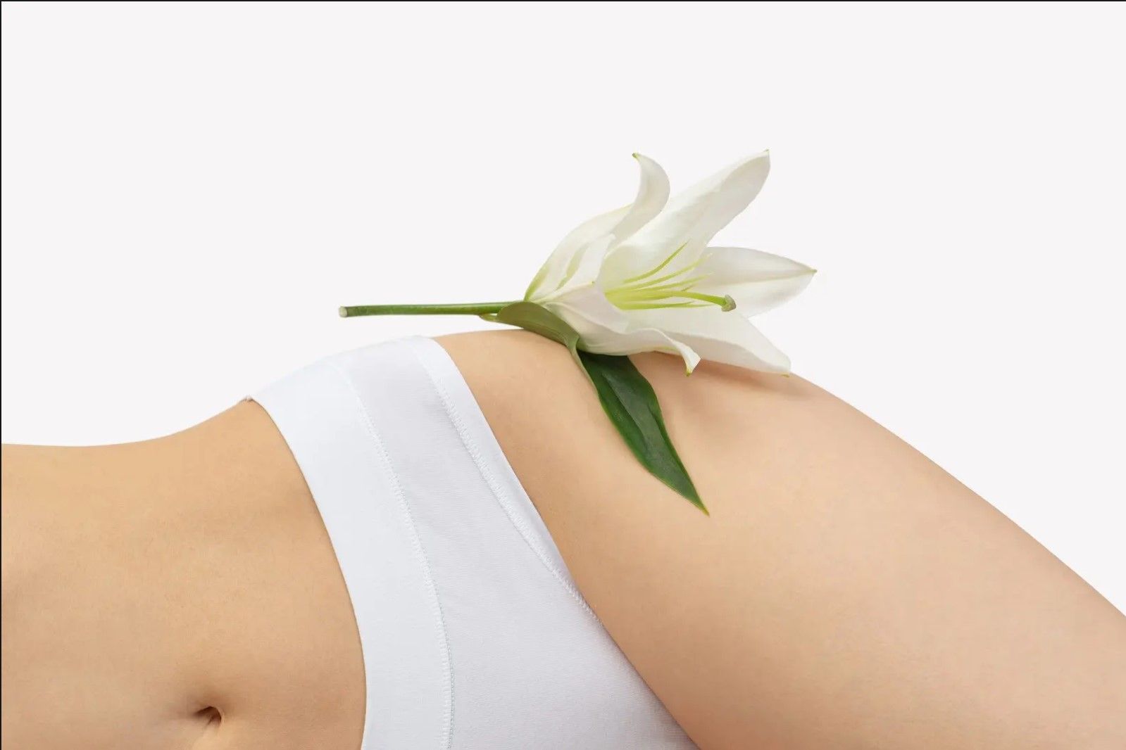 Woman in white underwear with a white lily flower resting on her hip. White background.