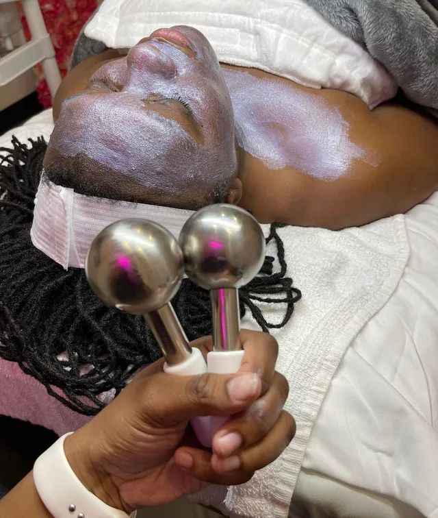 Person receiving a facial treatment with a light-colored mask. A hand holds two silver wands nearby.