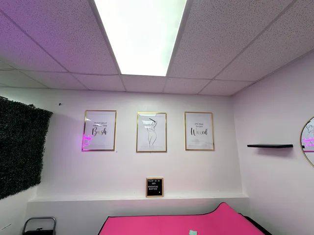 Interior with three framed art prints and a pink surface. The wall is white with a black framed sign and a black shelf.