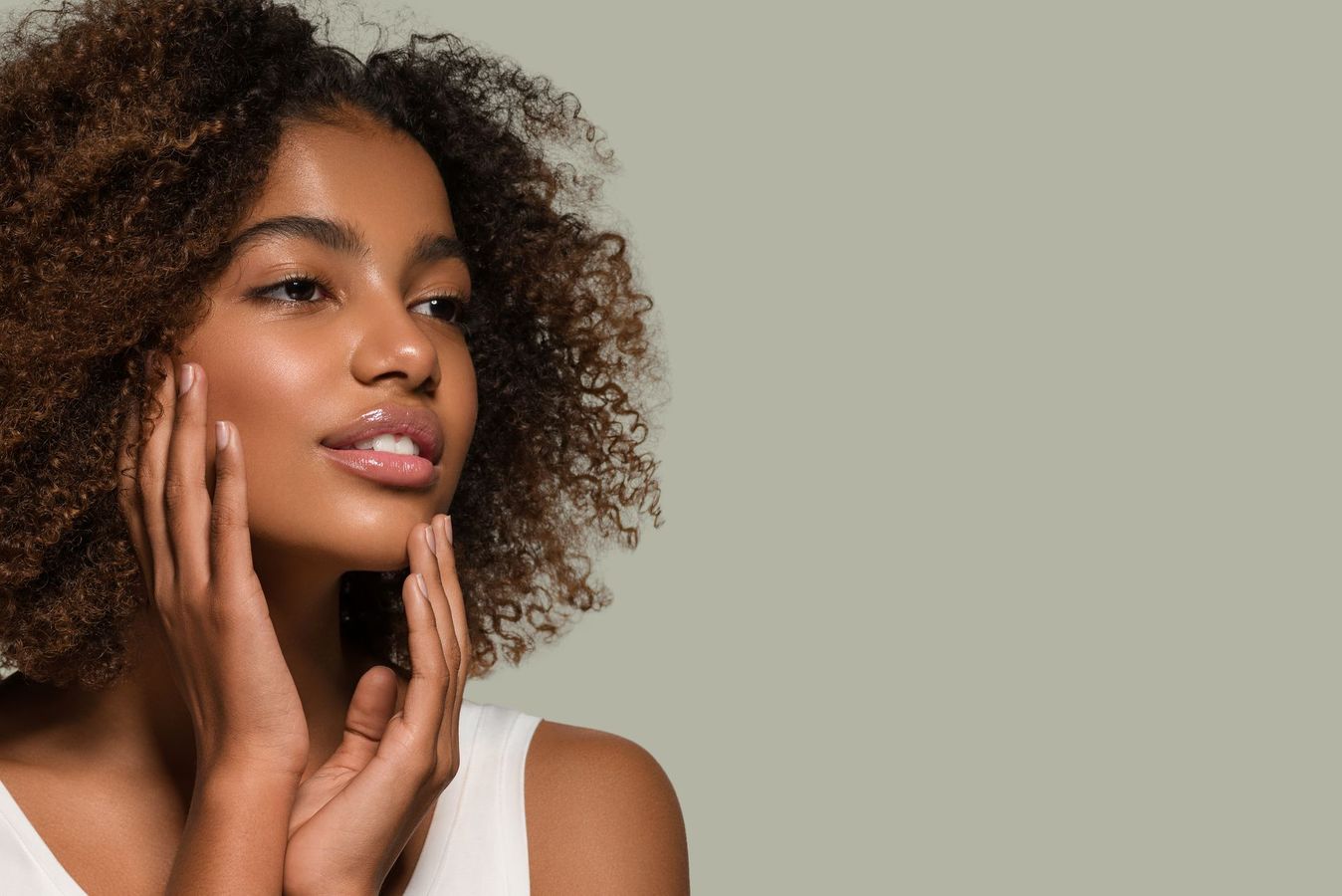 A woman with curly hair is touching her face.