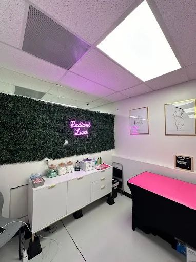 A beauty treatment room with a white cabinet, pink massage table, and a neon sign reading 