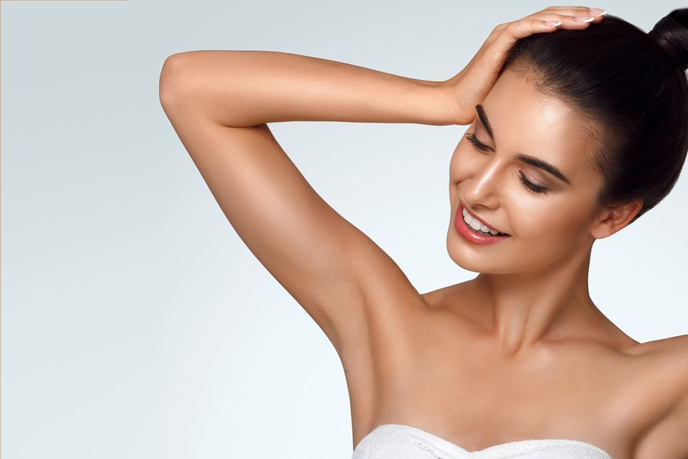 A woman is smiling and holding her hair in a bun.