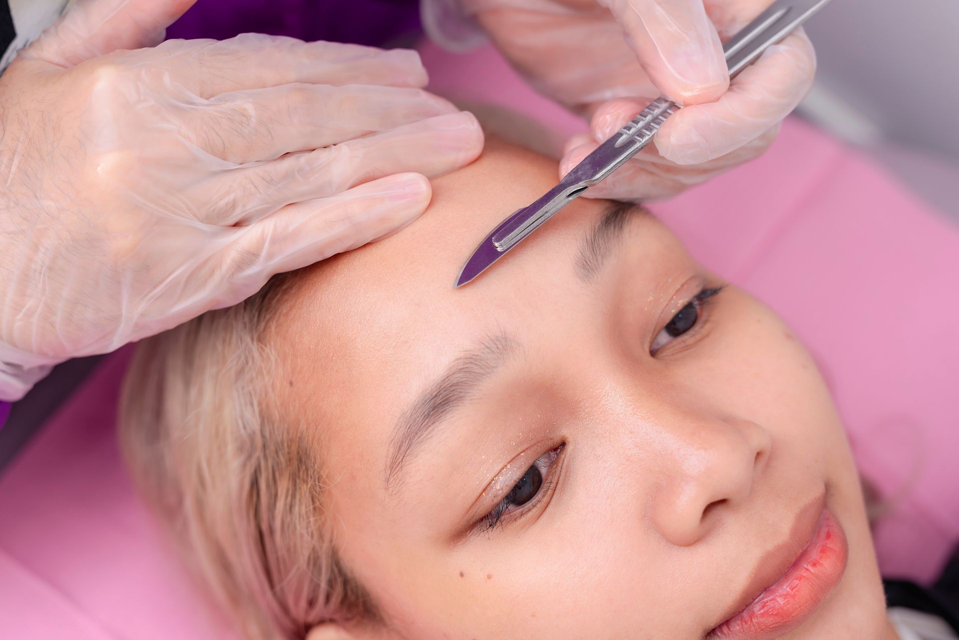 A woman is getting a dermaplaning service on her forehead.