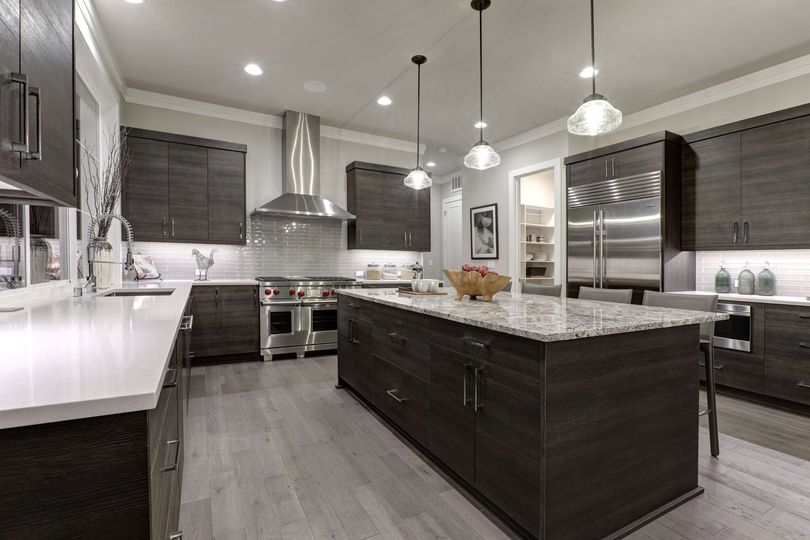 Modern kitchen with dark wood cabinetry, a large granite island, stainless steel appliances, and light gray flooring.