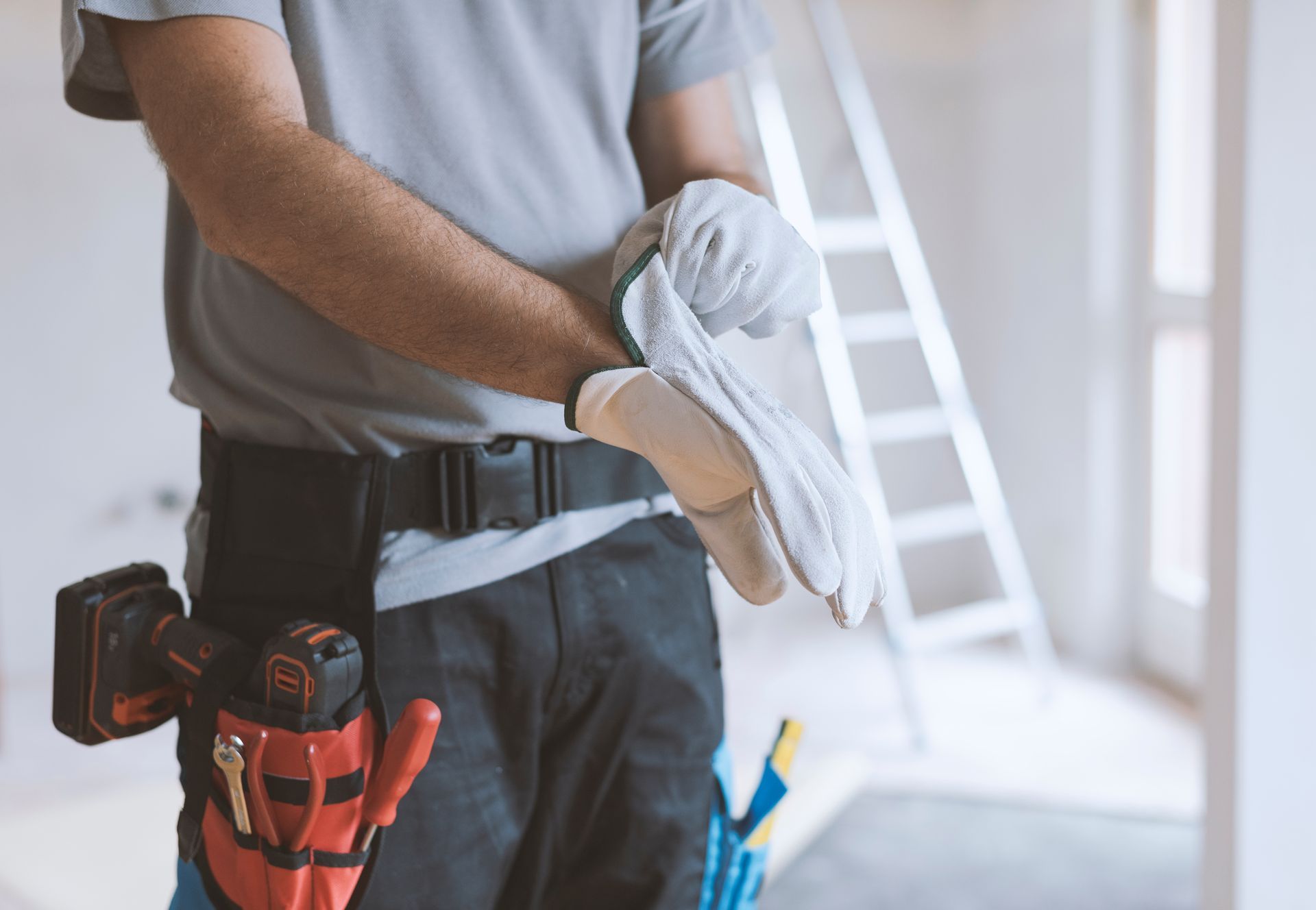 Worker holding folded white cloths at a construction site, with tools in a belt and a ladder in the background