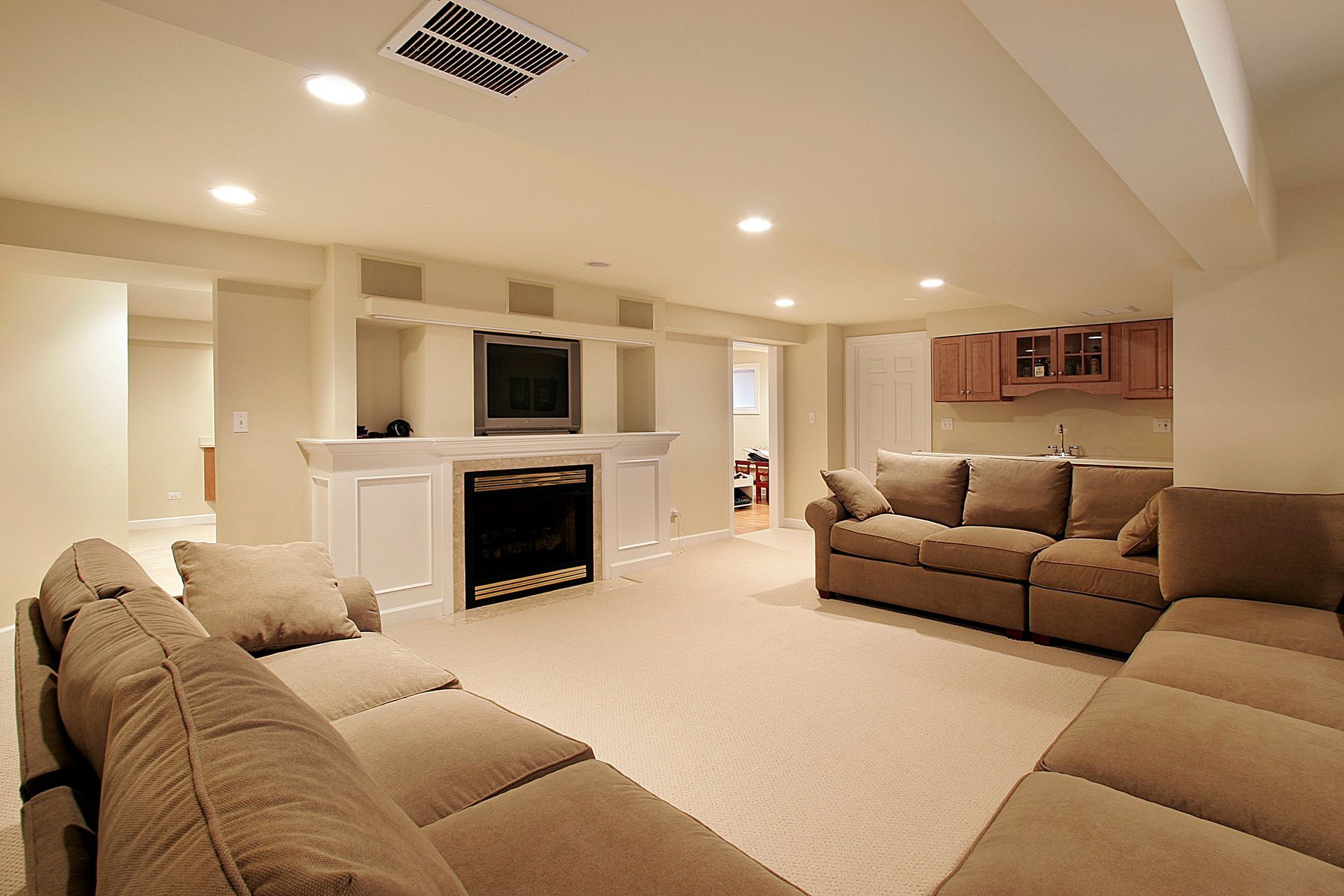 A neutral-toned basement featuring a large sectional sofa facing a built-in fireplace with an integrated TV and shelving.