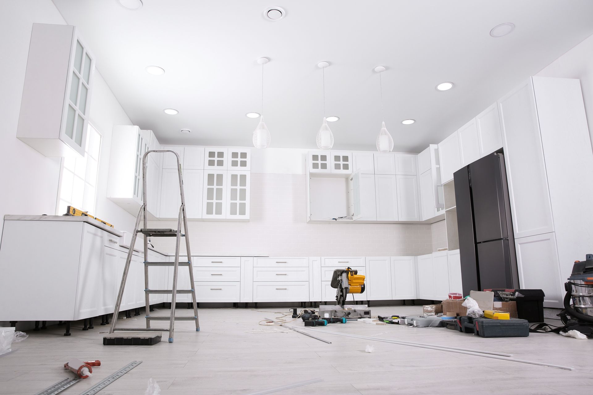 Bright white kitchen under renovation with cabinets, ladder, and tools scattered on the floor