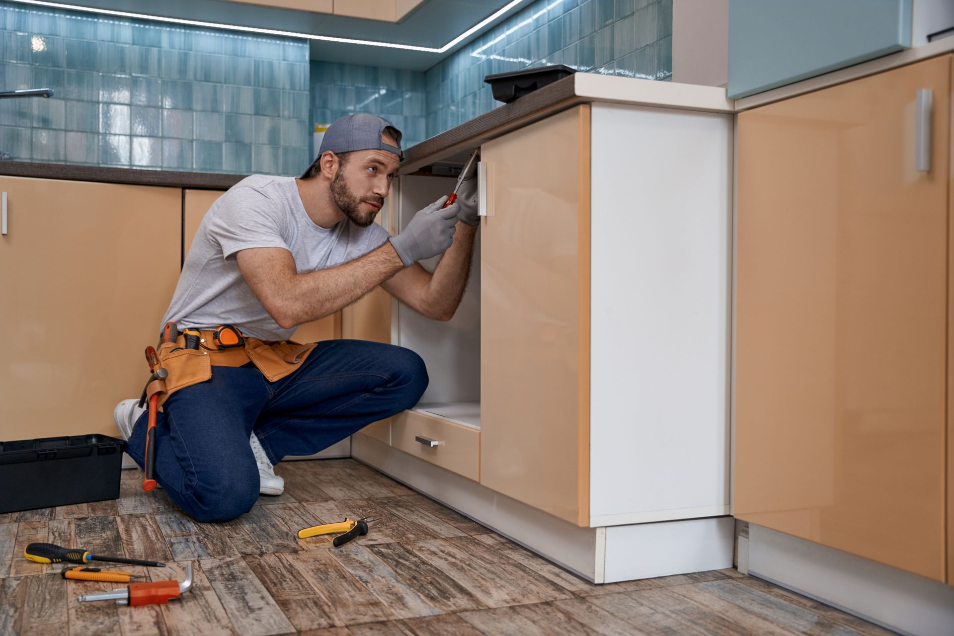 Technician kneeling in a kitchen, fixing a cabinet with tools on the floor.