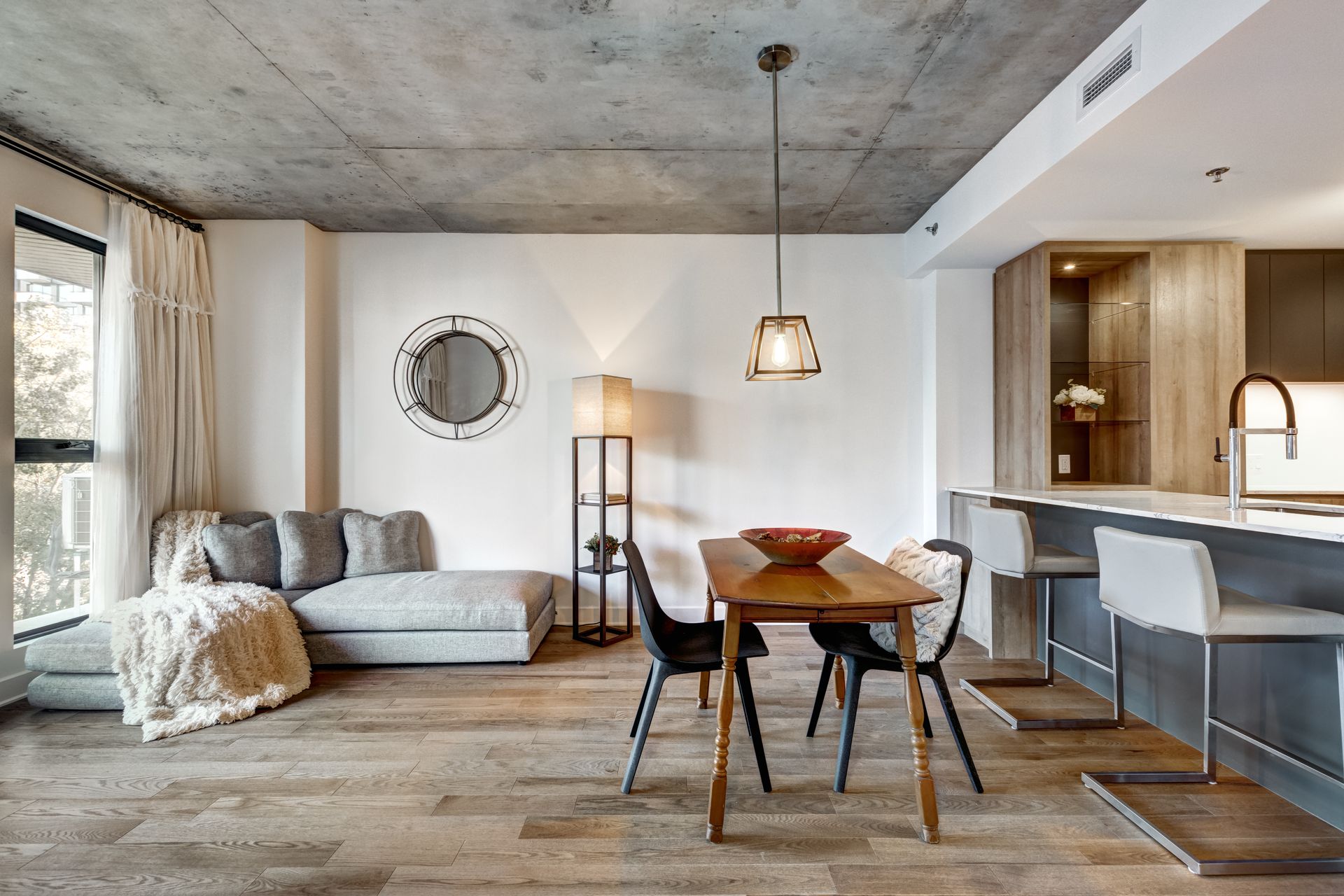 Modern open-plan living room with gray sofa, round dining table, and kitchen bar in a bright neutral interior