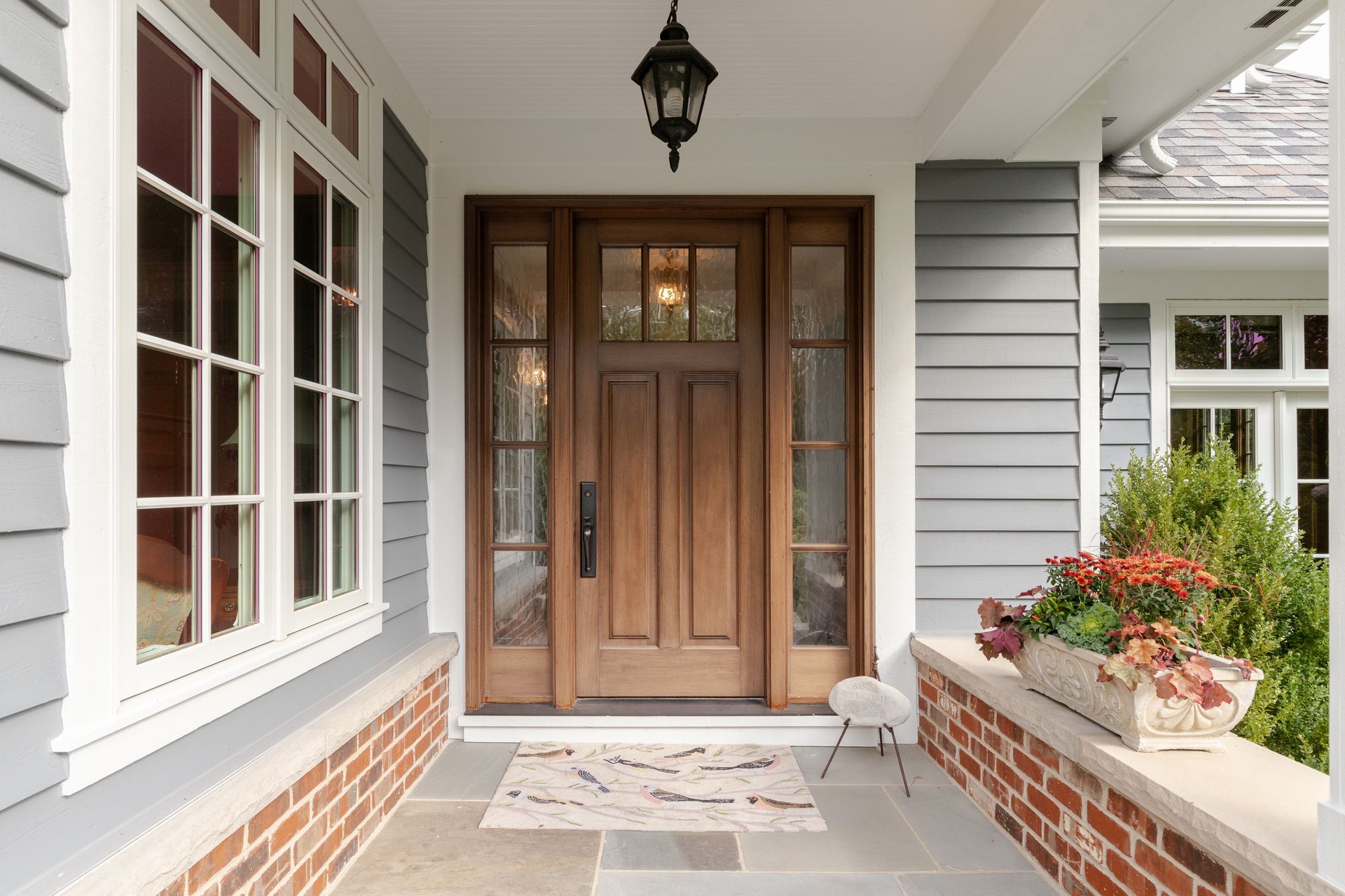 Front porch with wooden double doors, white siding, brick planters, and a hanging lantern Front porch with wooden double doors, white siding, brick planters, and a hanging lantern
