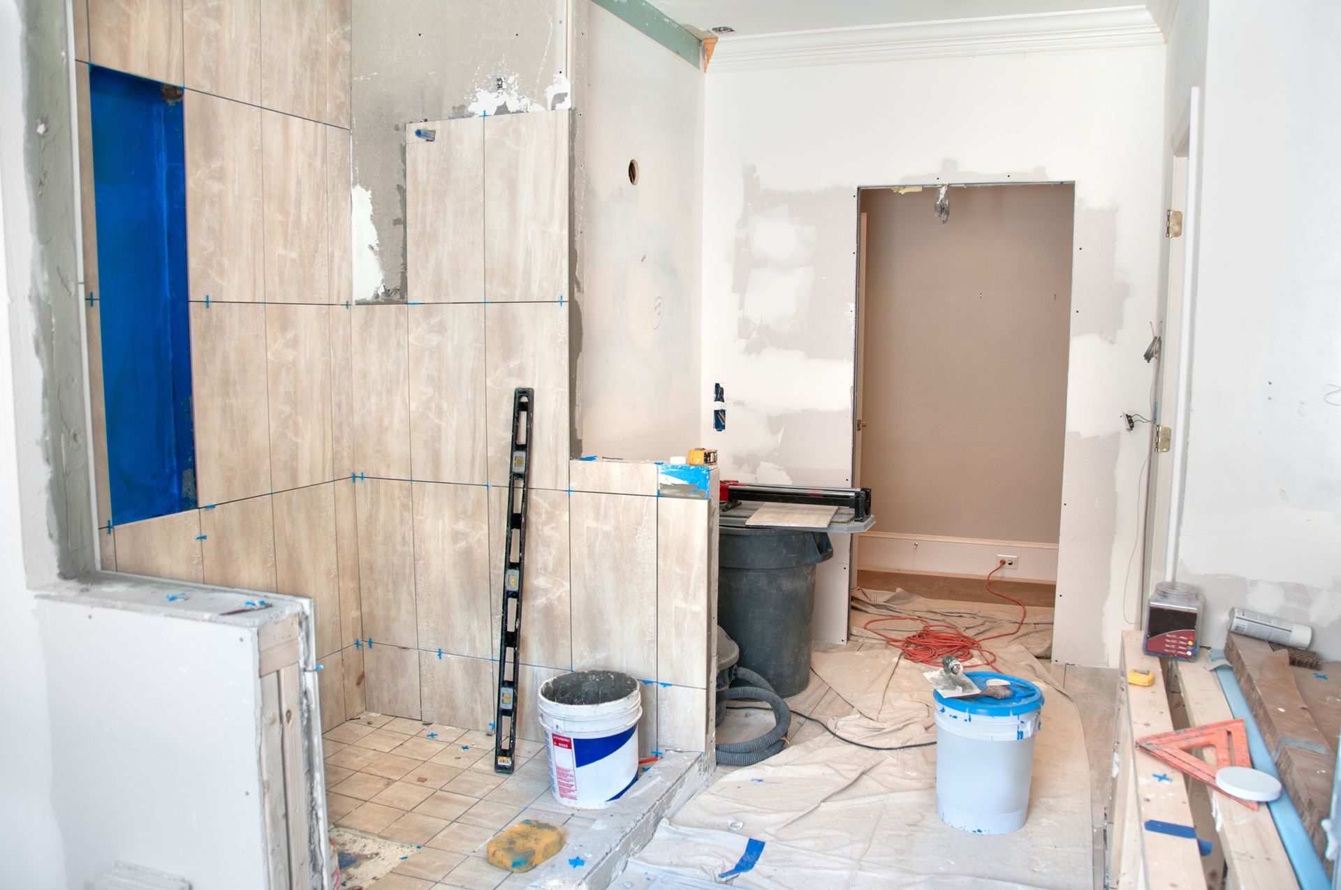 A bathroom undergoing renovation with tiled shower walls, a level, two buckets, and construction tools on the floor.