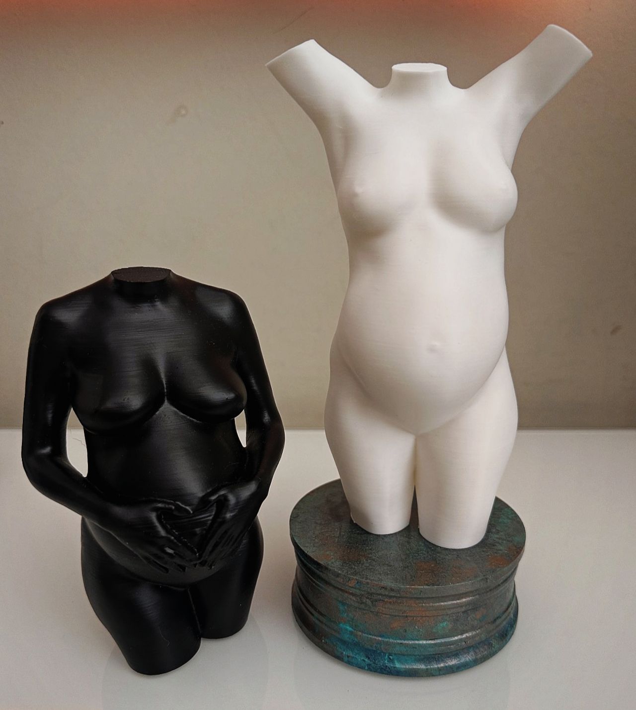 Twee torso-mannequins, een zwarte en een witte, tentoongesteld op gestapelde ronde sokkels.