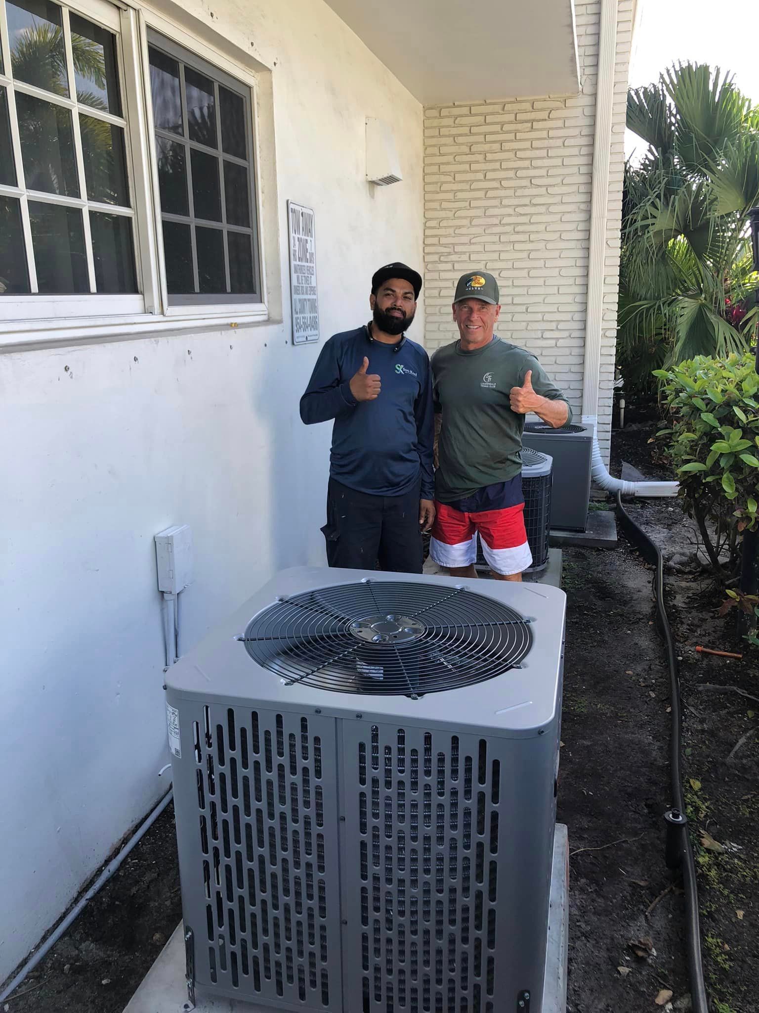 Two men are standing next to a large air conditioner and giving a thumbs up.