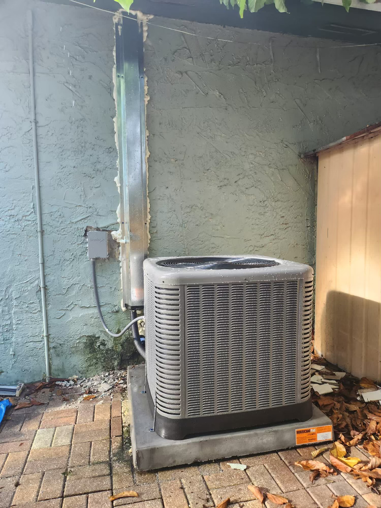 An air conditioner is sitting on a brick patio next to a wall.