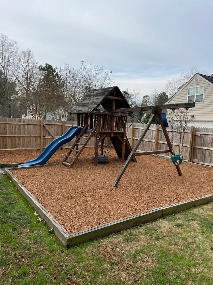 A wooden playground with a slide and swings in a backyard.