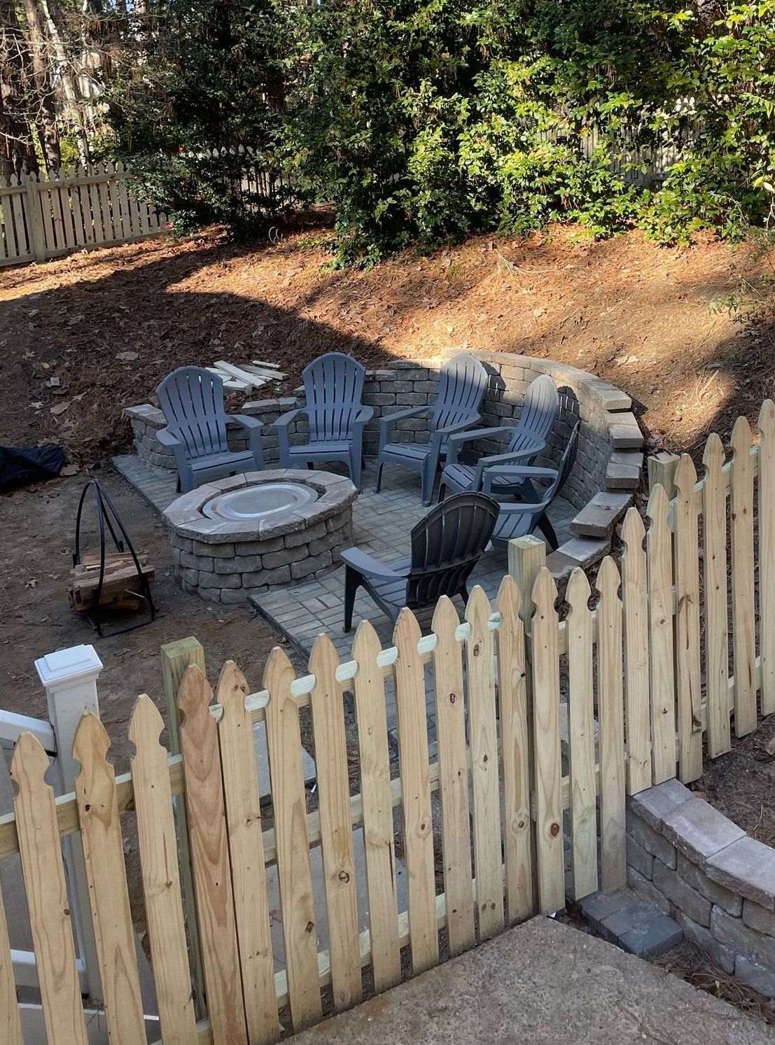 A wooden fence surrounds a fire pit in a backyard.