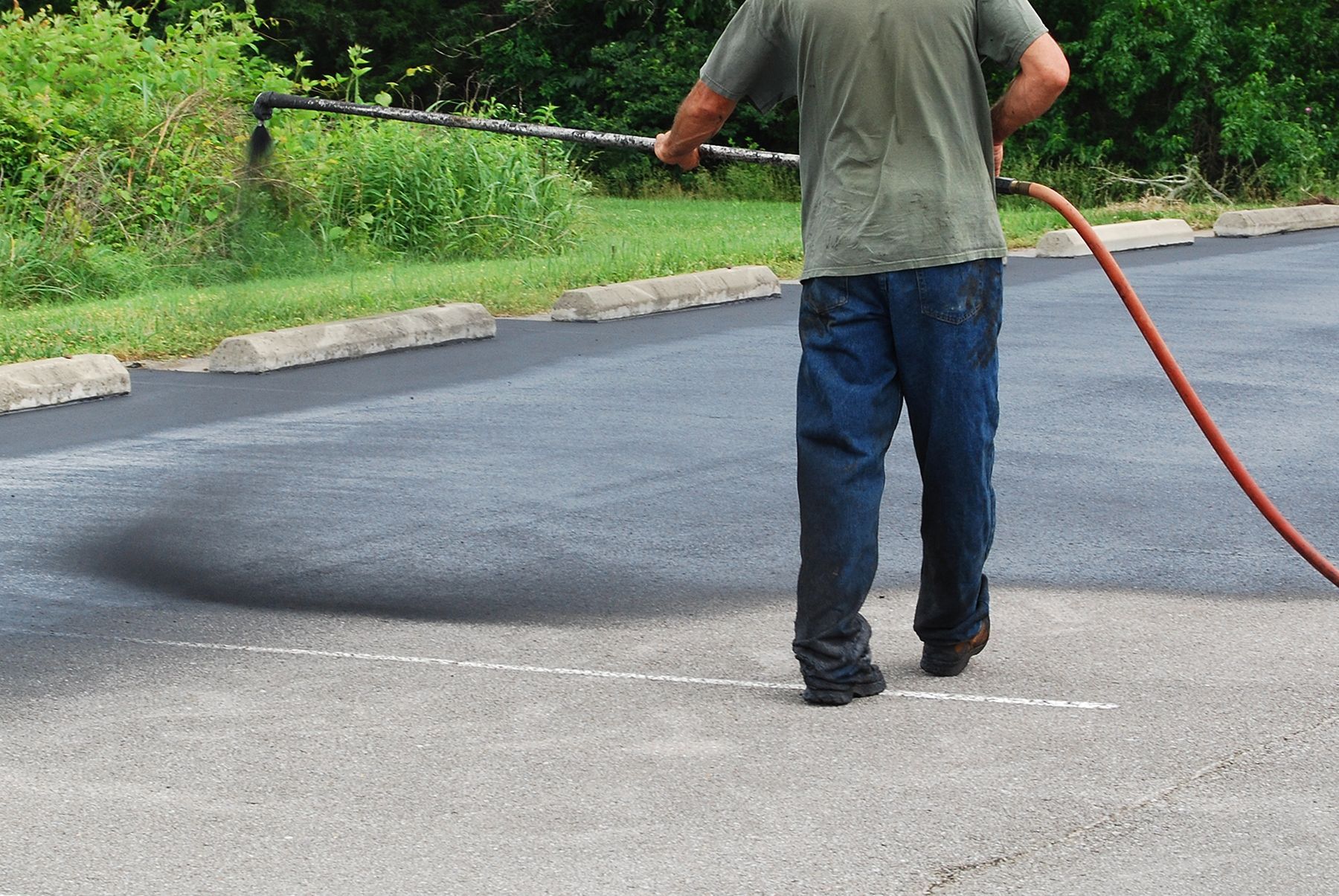 Specialist spraying a new sealer coat on an asphalt parking lot.