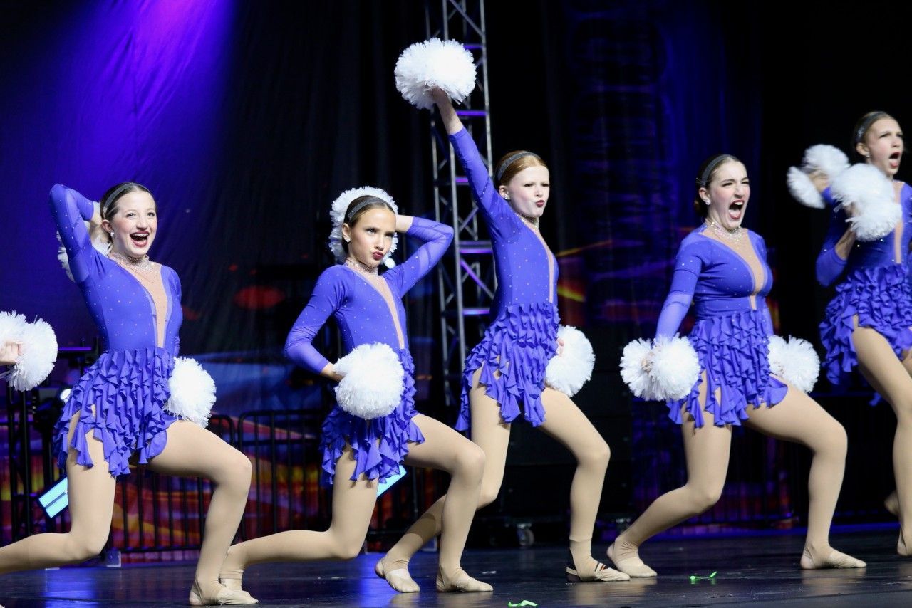 A group of cheerleaders are performing on a stage holding pom poms.