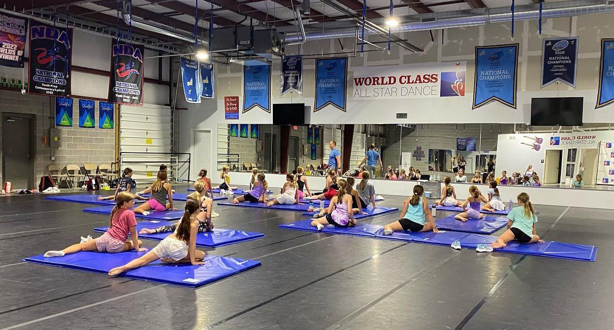 A group of young girls are doing stretching exercises on mats in a gym.
