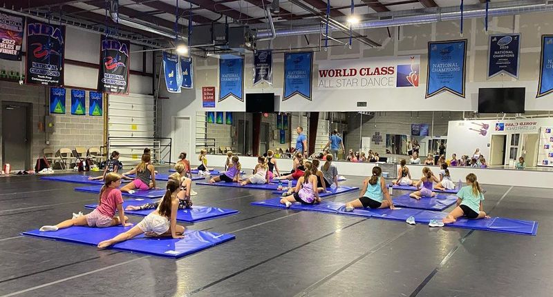 A group of young girls are doing stretching exercises on mats in a gym.